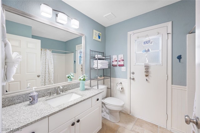 full bathroom featuring toilet, vanity, a shower with shower curtain, and wainscoting