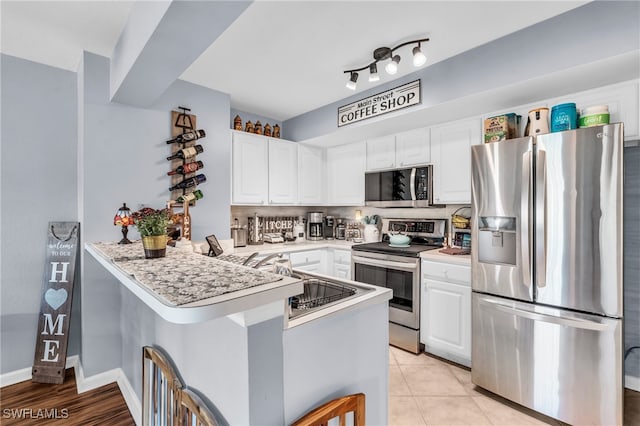 kitchen featuring kitchen peninsula, appliances with stainless steel finishes, light tile patterned floors, and white cabinetry