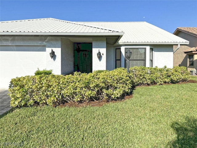 view of front of house with a garage, a front yard, metal roof, and stucco siding