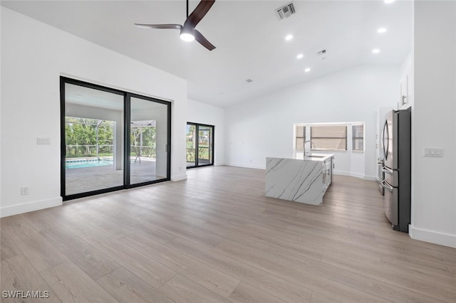 unfurnished living room with ceiling fan, a healthy amount of sunlight, light wood-type flooring, and high vaulted ceiling