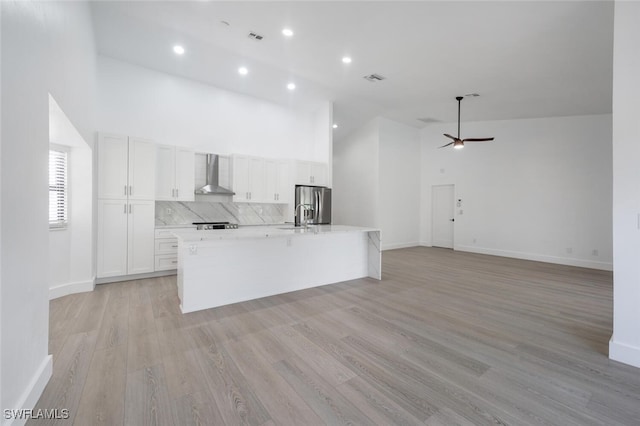 kitchen with high vaulted ceiling, white cabinets, wall chimney range hood, stainless steel fridge, and light hardwood / wood-style floors