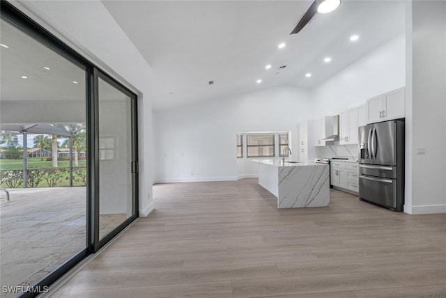 kitchen featuring light stone countertops, stainless steel refrigerator with ice dispenser, white cabinetry, and a wealth of natural light