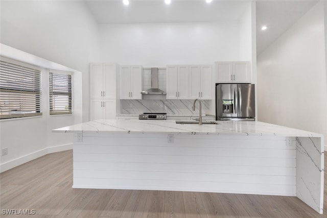 kitchen featuring appliances with stainless steel finishes, light wood-type flooring, sink, wall chimney range hood, and white cabinets