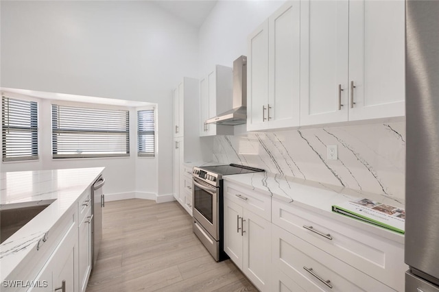 kitchen featuring white cabinets, wall chimney exhaust hood, light stone countertops, appliances with stainless steel finishes, and a healthy amount of sunlight