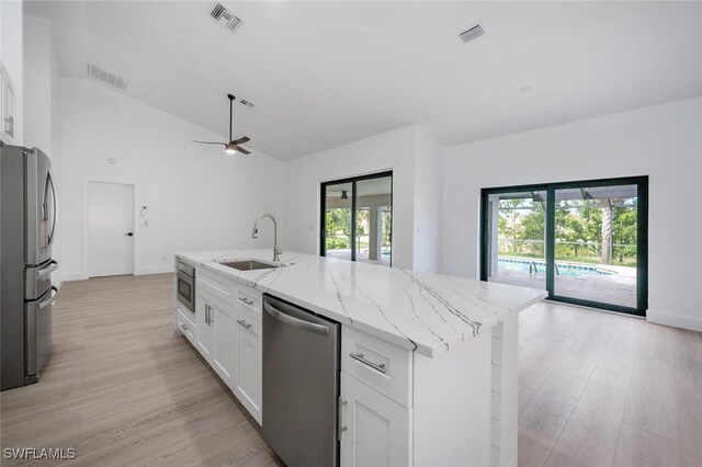 kitchen featuring sink, light stone counters, an island with sink, white cabinets, and appliances with stainless steel finishes