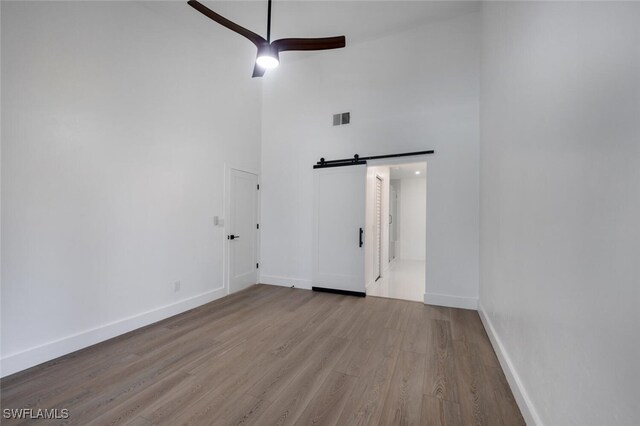 empty room with a high ceiling, a barn door, light hardwood / wood-style flooring, and ceiling fan