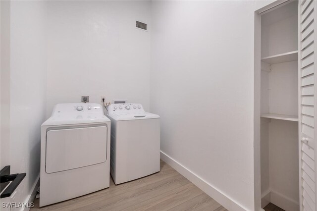 clothes washing area featuring washer and clothes dryer and light wood-type flooring