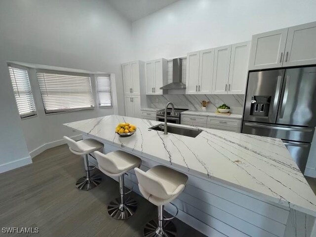 kitchen featuring a kitchen bar, wall chimney exhaust hood, stainless steel appliances, sink, and high vaulted ceiling