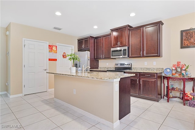 kitchen featuring an island with sink, stainless steel appliances, light tile patterned floors, and light stone countertops