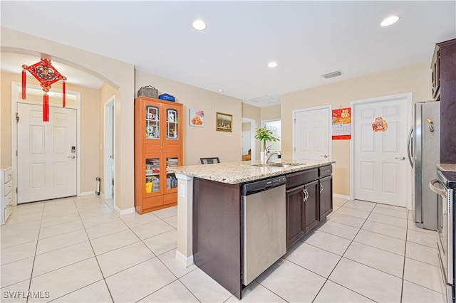 kitchen featuring appliances with stainless steel finishes, light tile patterned floors, dark brown cabinetry, a center island with sink, and sink