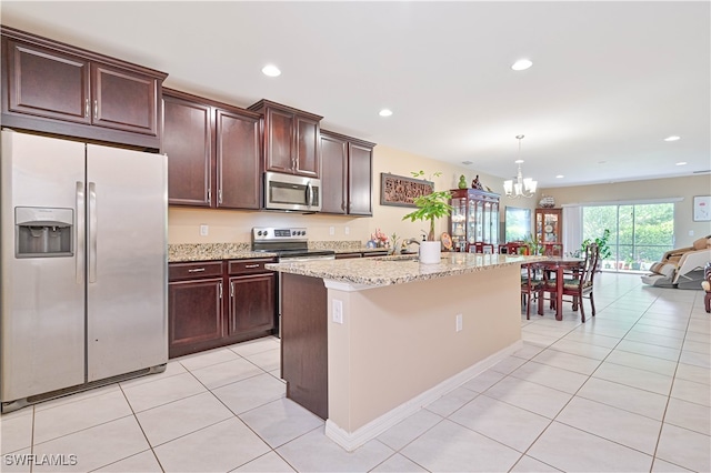 kitchen with appliances with stainless steel finishes, hanging light fixtures, light stone countertops, an inviting chandelier, and a kitchen island with sink