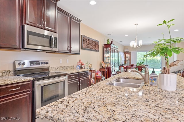 kitchen with sink, a notable chandelier, hanging light fixtures, appliances with stainless steel finishes, and light stone countertops