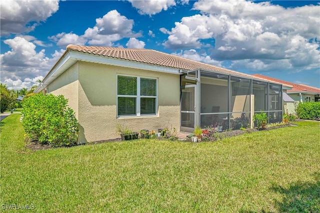 rear view of property featuring a yard, a tile roof, and stucco siding