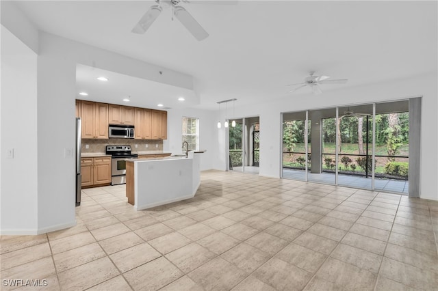 kitchen featuring sink, backsplash, a center island with sink, appliances with stainless steel finishes, and ceiling fan