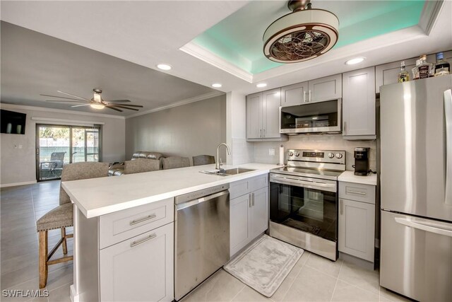 kitchen featuring a tray ceiling, kitchen peninsula, gray cabinetry, stainless steel appliances, and ceiling fan