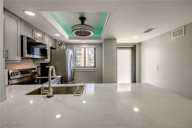 kitchen with gray cabinets, light stone counters, a tray ceiling, stainless steel appliances, and crown molding