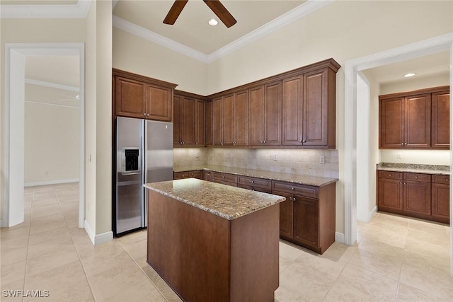 kitchen featuring crown molding, a center island, stainless steel fridge, light stone countertops, and decorative backsplash