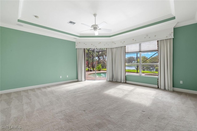 empty room with a tray ceiling, ornamental molding, and carpet flooring