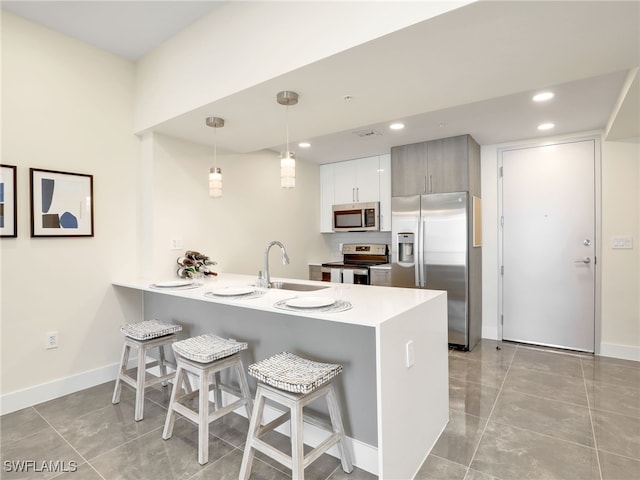 kitchen featuring kitchen peninsula, appliances with stainless steel finishes, a kitchen breakfast bar, sink, and decorative light fixtures