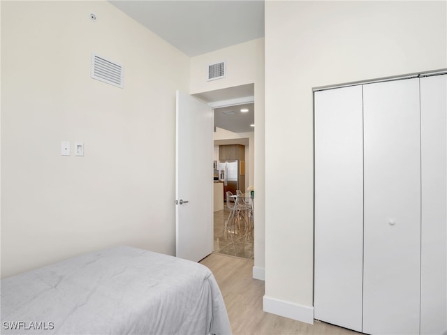 bedroom featuring stainless steel fridge, a closet, and light hardwood / wood-style flooring