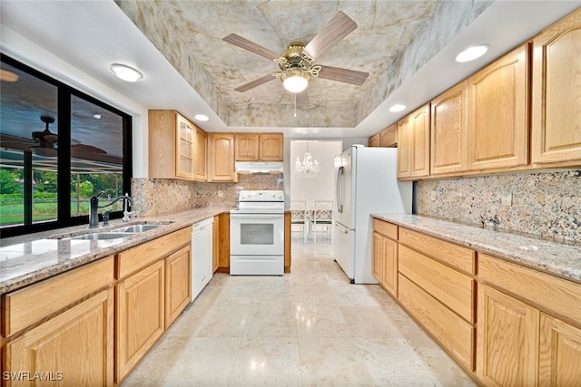 kitchen featuring light stone counters, sink, ceiling fan with notable chandelier, white appliances, and a raised ceiling