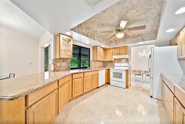 kitchen featuring tasteful backsplash, ceiling fan with notable chandelier, kitchen peninsula, white appliances, and a raised ceiling