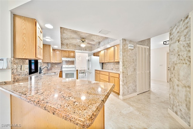 kitchen featuring light stone counters, sink, kitchen peninsula, white appliances, and ceiling fan