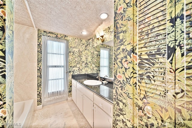 bathroom with a textured ceiling, vanity, and a tub