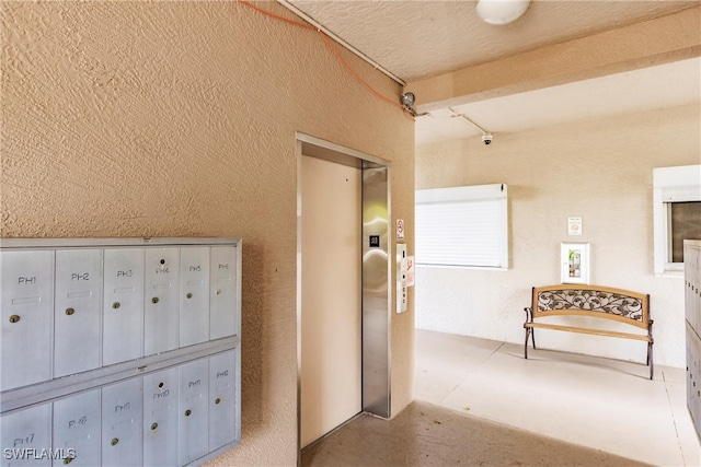 corridor with mail area, elevator, and a textured wall