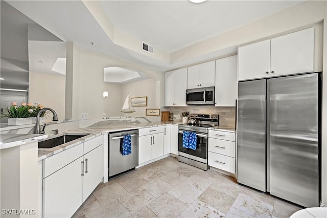 kitchen with white cabinetry, stainless steel appliances, sink, kitchen peninsula, and light stone counters