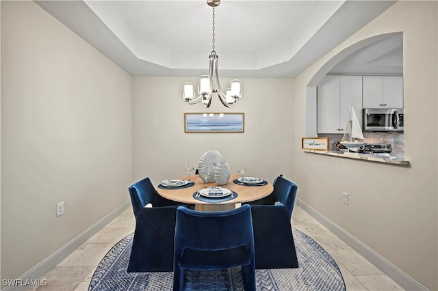 dining space featuring light tile patterned floors, an inviting chandelier, and a tray ceiling