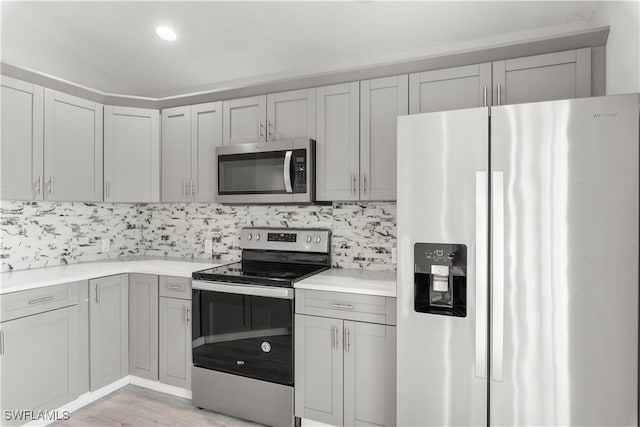 kitchen with light wood-type flooring, gray cabinets, stainless steel appliances, and tasteful backsplash