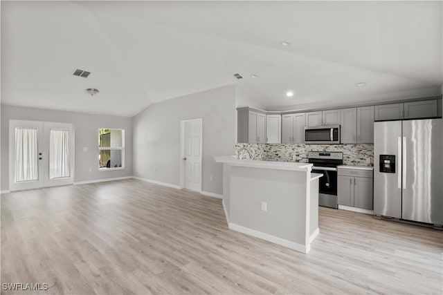 kitchen with appliances with stainless steel finishes, gray cabinetry, vaulted ceiling, tasteful backsplash, and light hardwood / wood-style flooring