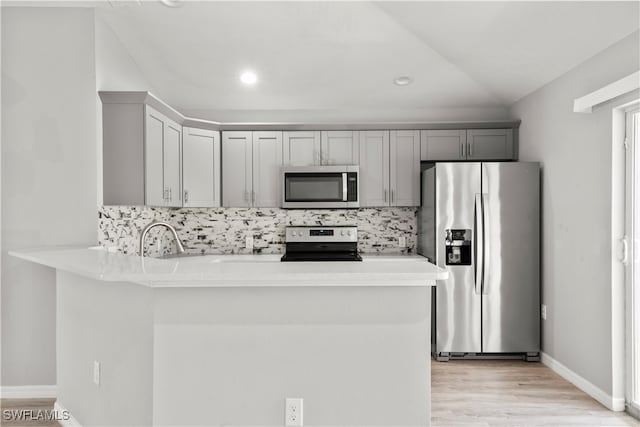 kitchen with appliances with stainless steel finishes, gray cabinetry, light hardwood / wood-style floors, backsplash, and kitchen peninsula