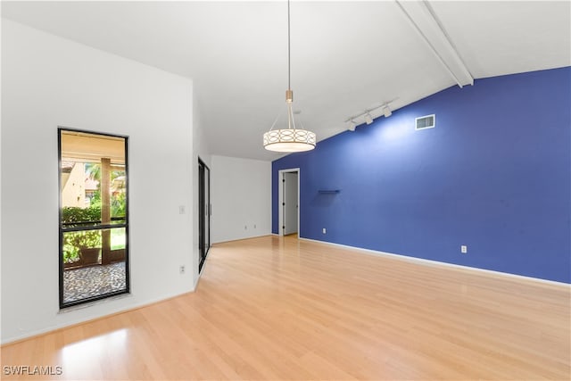 empty room featuring light wood-type flooring, vaulted ceiling with beams, and track lighting