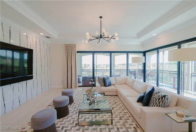 living room with a tray ceiling, light hardwood / wood-style flooring, ornamental molding, and an inviting chandelier