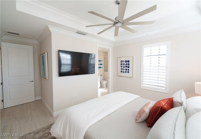 bedroom featuring ensuite bath, ceiling fan, a raised ceiling, crown molding, and light wood-type flooring