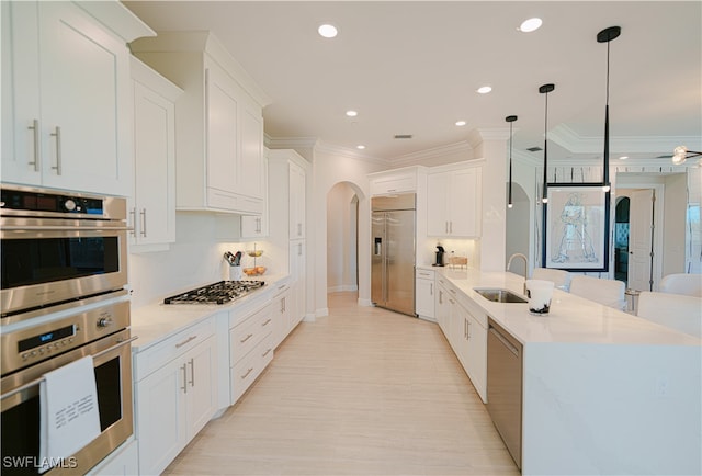 kitchen featuring pendant lighting, white cabinets, sink, ornamental molding, and appliances with stainless steel finishes