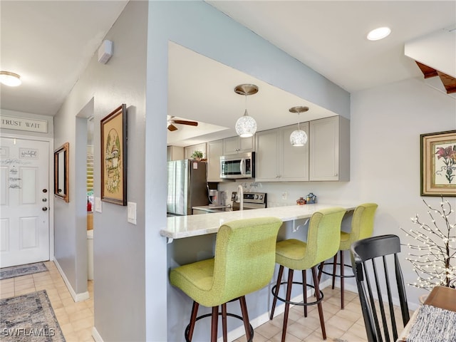 kitchen with appliances with stainless steel finishes, kitchen peninsula, a breakfast bar area, gray cabinets, and ceiling fan