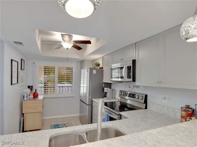 kitchen with ceiling fan with notable chandelier, stainless steel appliances, a raised ceiling, and white cabinetry