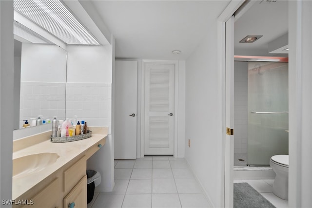 bathroom with tile patterned flooring, toilet, tile walls, a shower with door, and vanity