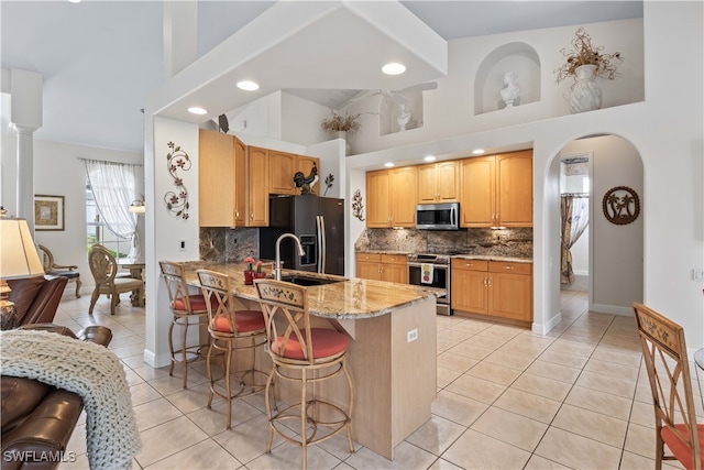 kitchen featuring a breakfast bar, kitchen peninsula, decorative backsplash, a towering ceiling, and appliances with stainless steel finishes