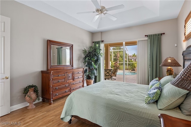 bedroom with light wood-type flooring, a tray ceiling, ceiling fan, and access to outside