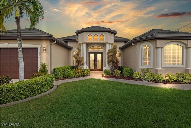 mediterranean / spanish-style home with a garage, a yard, and french doors