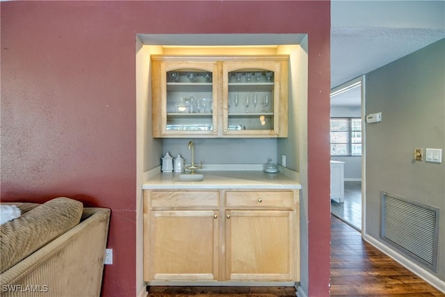 bar featuring light brown cabinets, dark hardwood / wood-style flooring, and sink