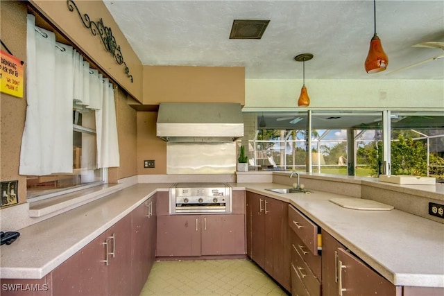 kitchen featuring cooktop, sink, pendant lighting, and wall chimney range hood