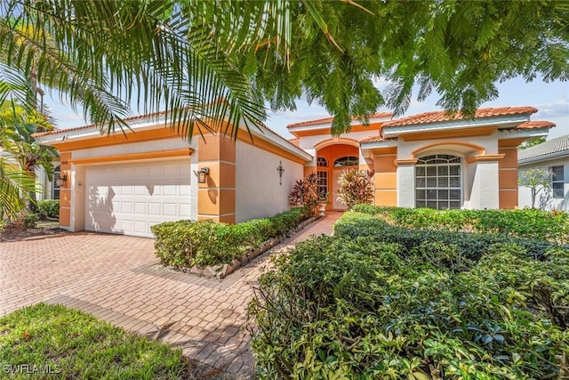 mediterranean / spanish-style house with stucco siding, a tiled roof, and decorative driveway