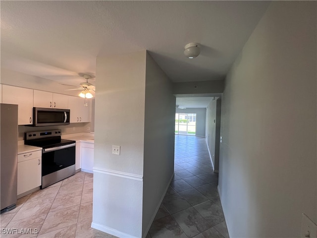 kitchen featuring ceiling fan, appliances with stainless steel finishes, light tile patterned floors, and white cabinetry