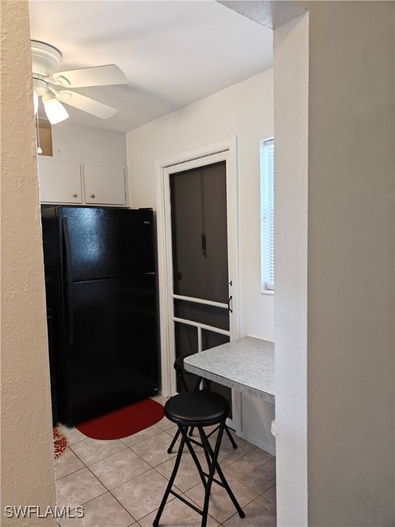 kitchen featuring white cabinets, light tile patterned floors, black refrigerator, and ceiling fan