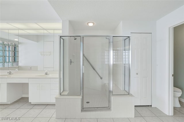 full bath with double vanity, toilet, a shower stall, and a textured ceiling